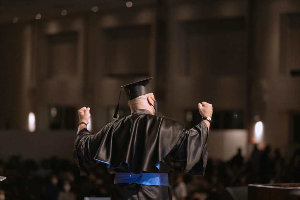 pexels-photo-11286592-11286592 Graduate celebrating success at ceremony with arms raised in joy.