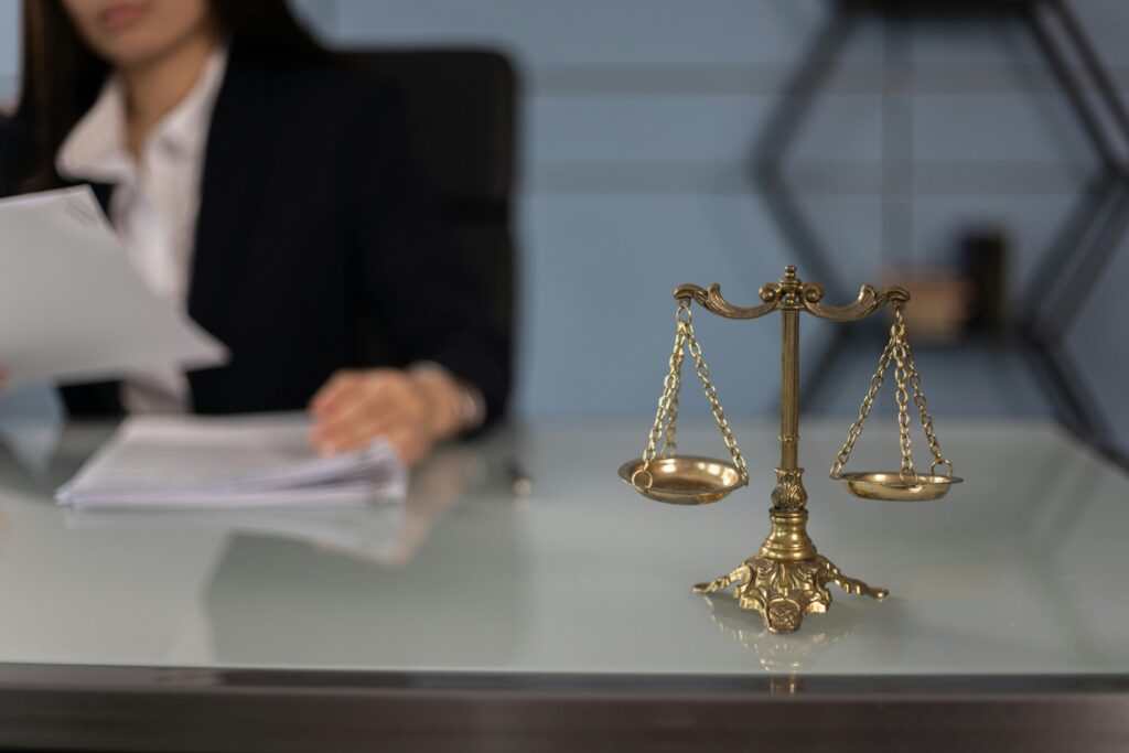 pexels-photo-6077520-6077520 Balance scales on a desk in a professional office with a blurred businesswoman in the background.